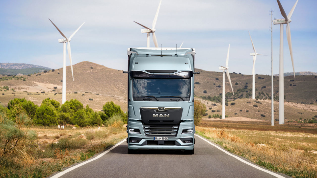 MAN eTruck driving through landscape with wind turbines in the background