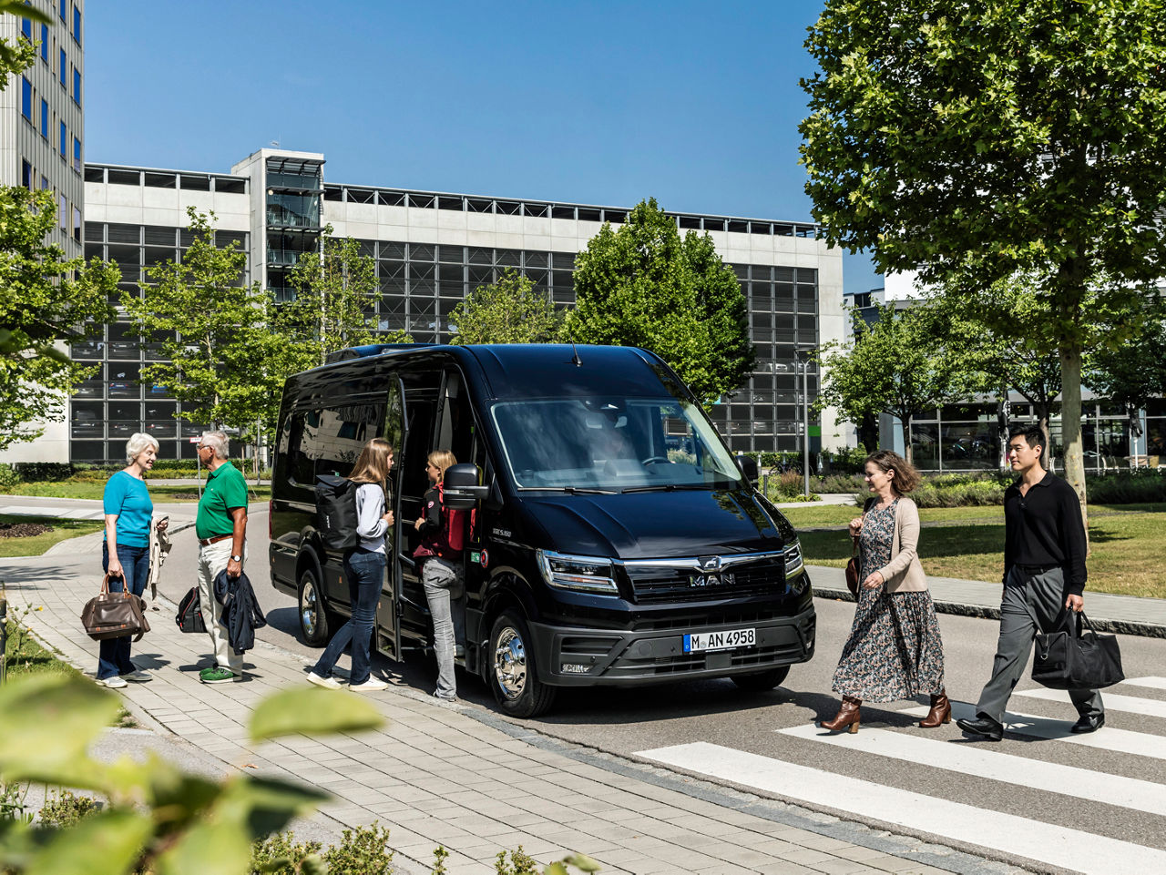 Minibus MAN TGE s cestujícími před kancelářskou budovou.