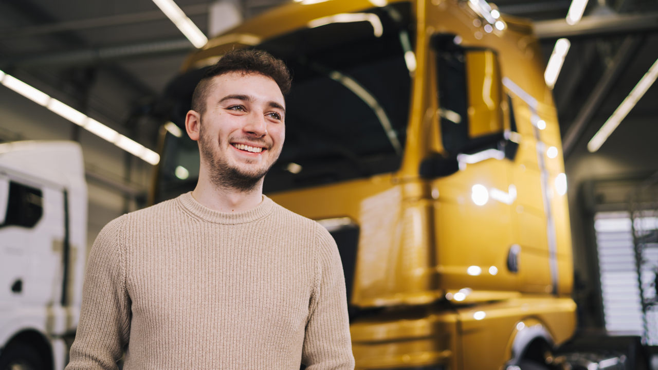 A young man stands in front of a truck
