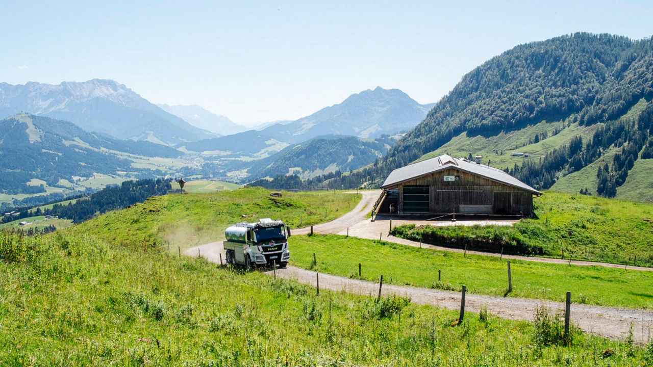 Blick über die Alm: Truck fährt an einer Almhütte vorbei
