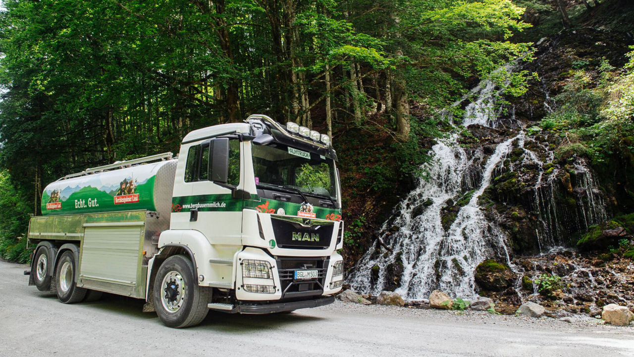 Almtruck fährt an einem Wasserfall vorbei