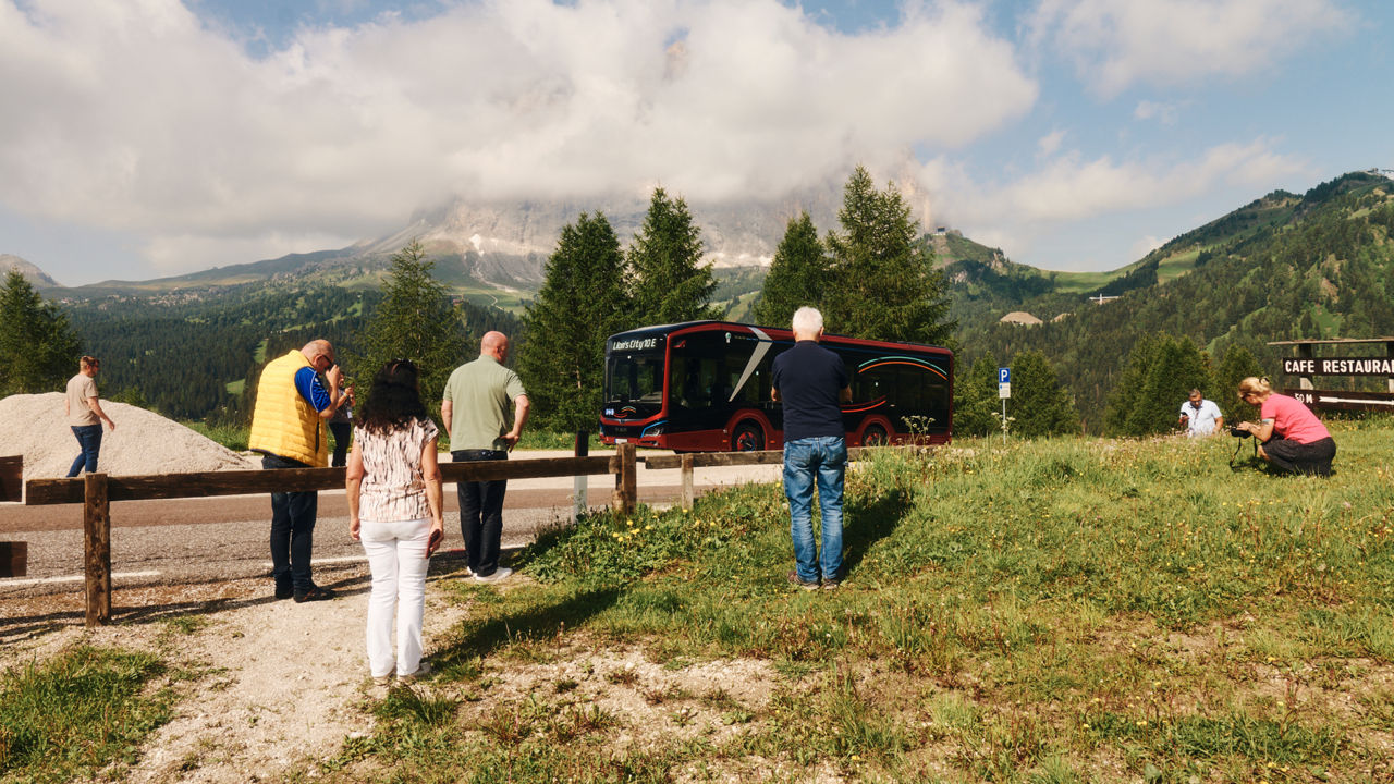 People standing in a meadow in the mountains taking pictures of a bus