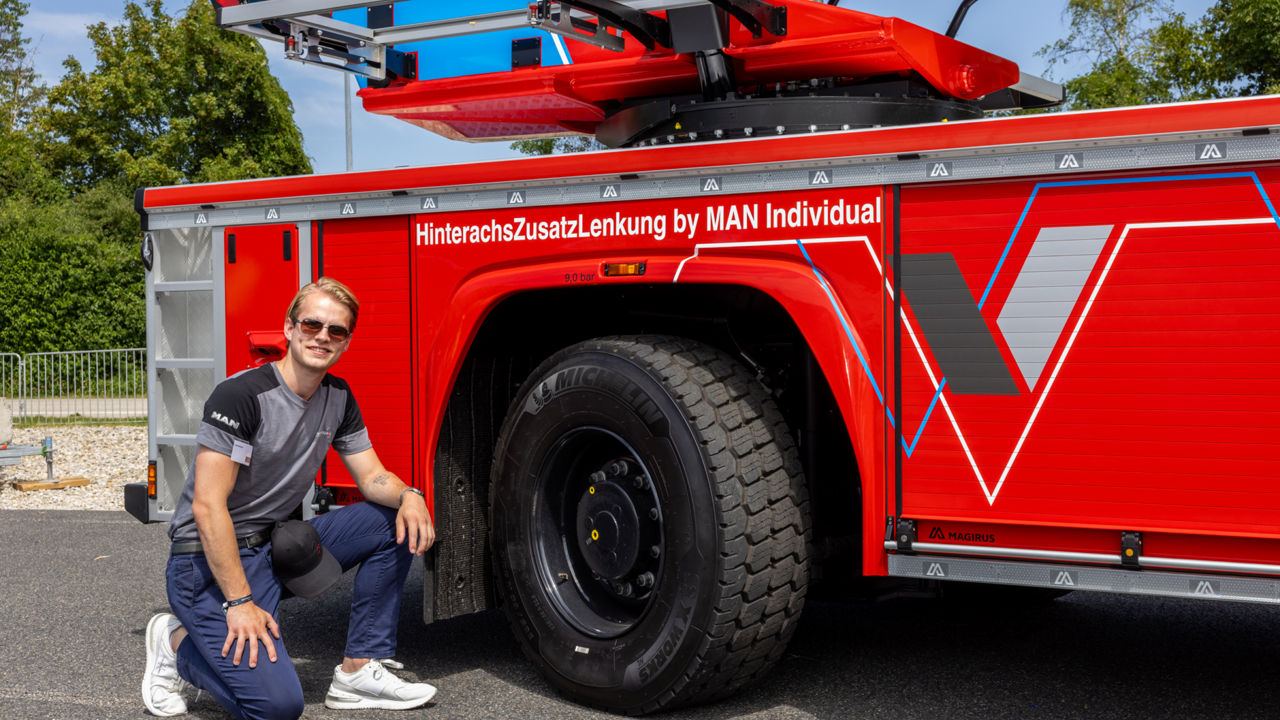 A man kneels in front of a red fire engine