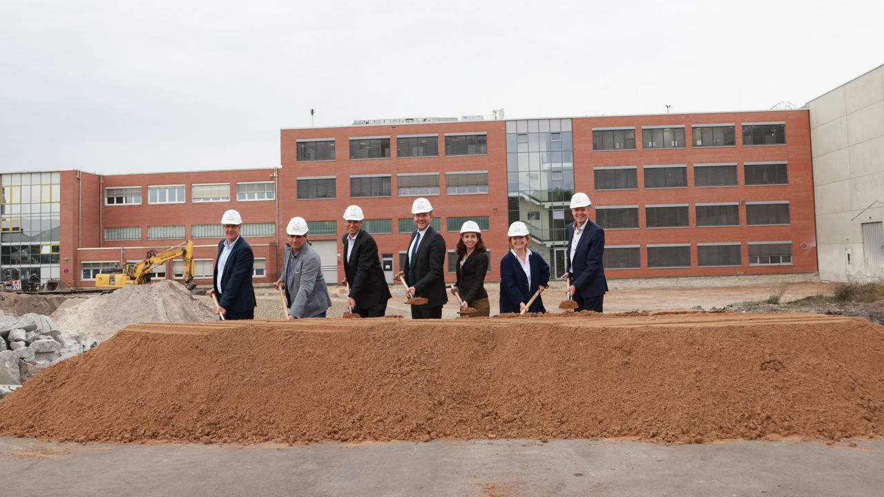 Die Projektverantwortlichen nehmen den ersten Spatenstich vor und stehen vor einem Erdhaufen