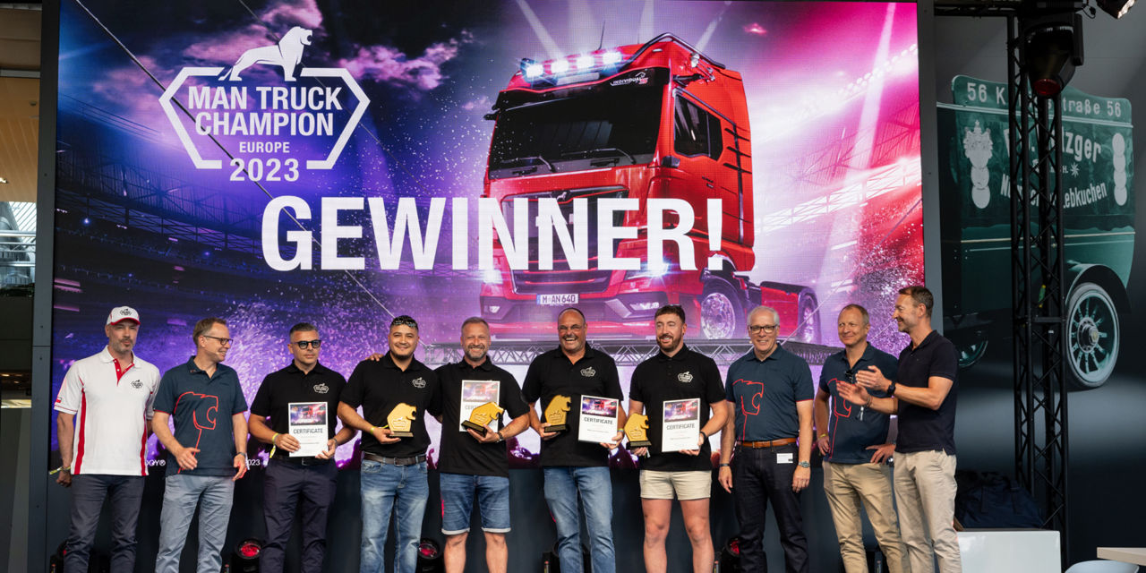 A group of men stand in front of a large screen that says "Winner"