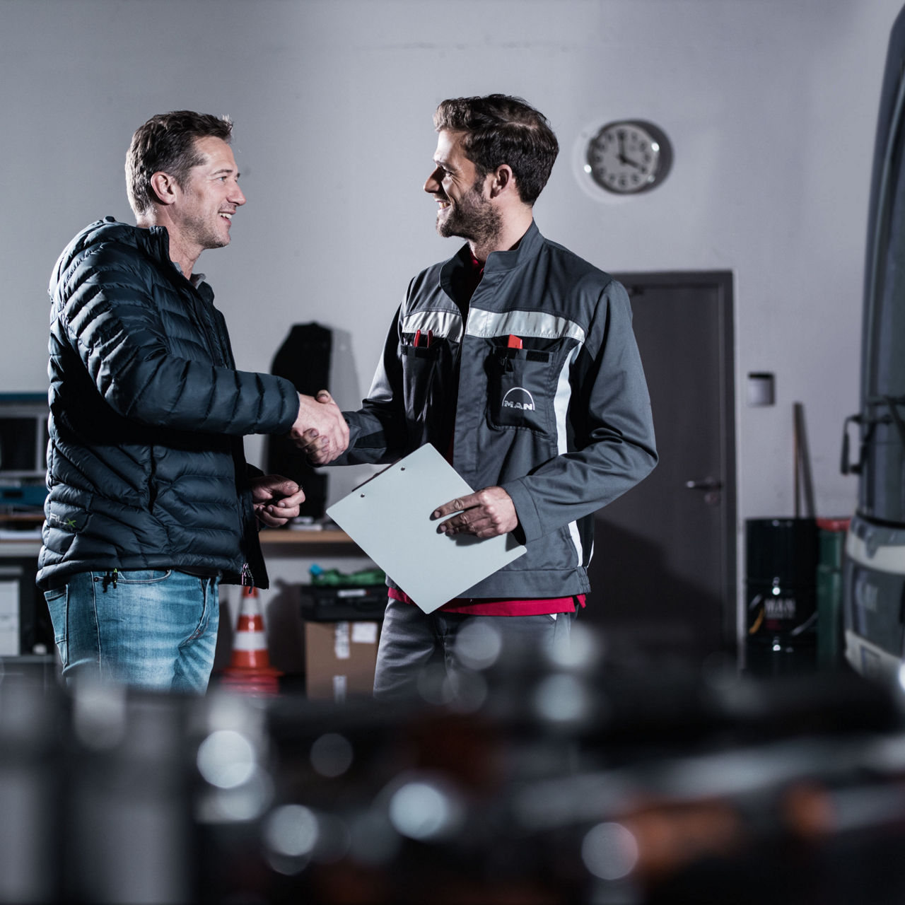 Un personnel du service après-vente serre la main à un client satisfait près d’un bus MAN, dans un atelier.