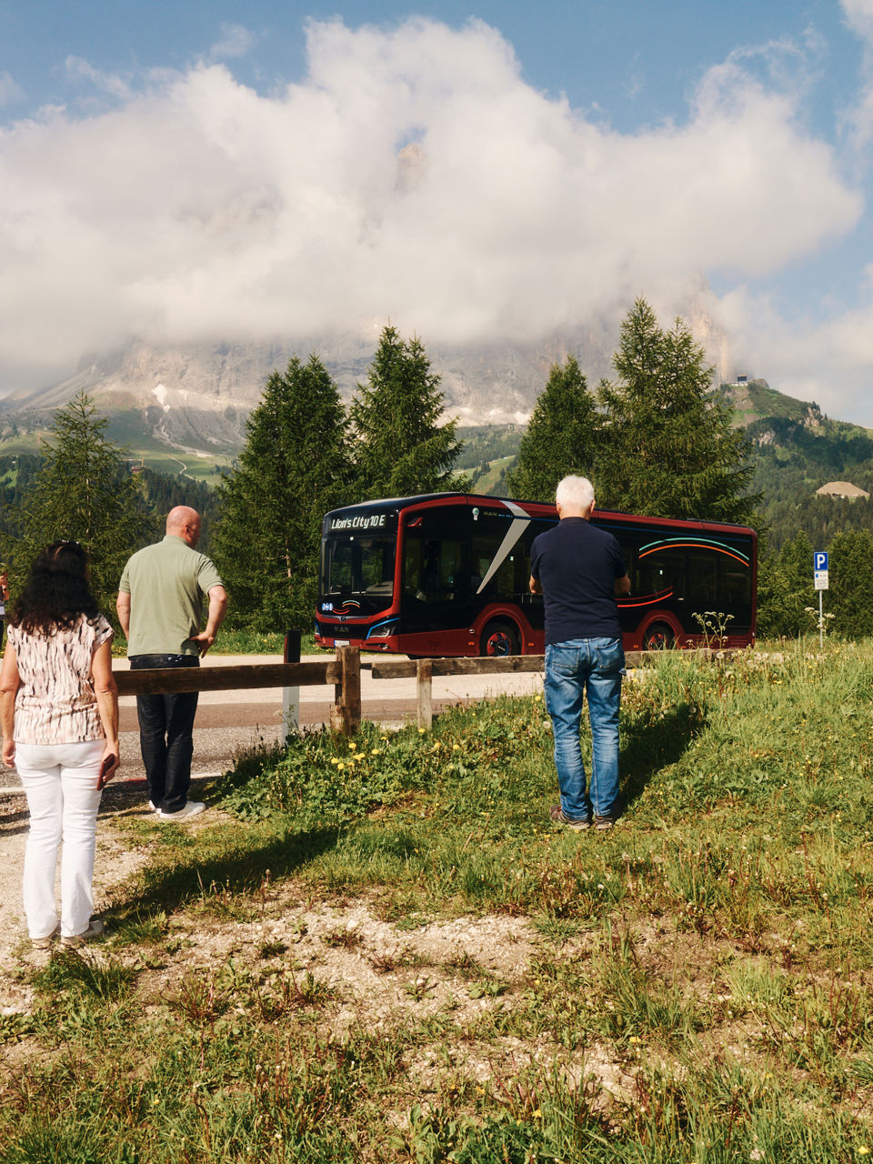 People standing in a meadow in the mountains taking pictures of a bus