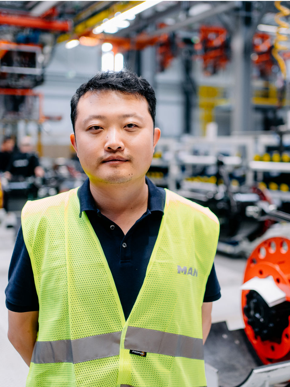 Ein Mann in Warnweste steht in einer Produktionshalle