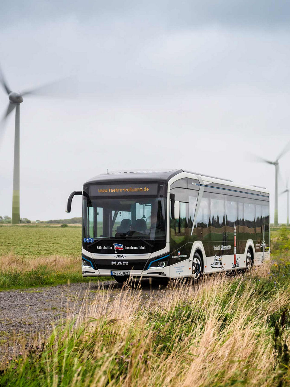 MAN Lion's City E on a green road and lots of wind turbines in the distance