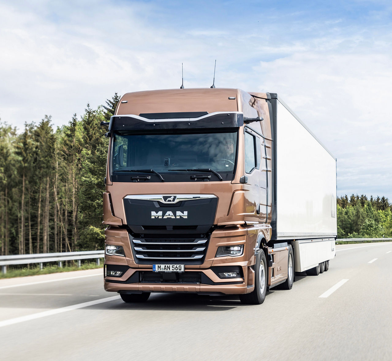 Bronzefarbener MAN TGX  Sattelzug fährt auf Autobahn durch bewaldete Landschaft.