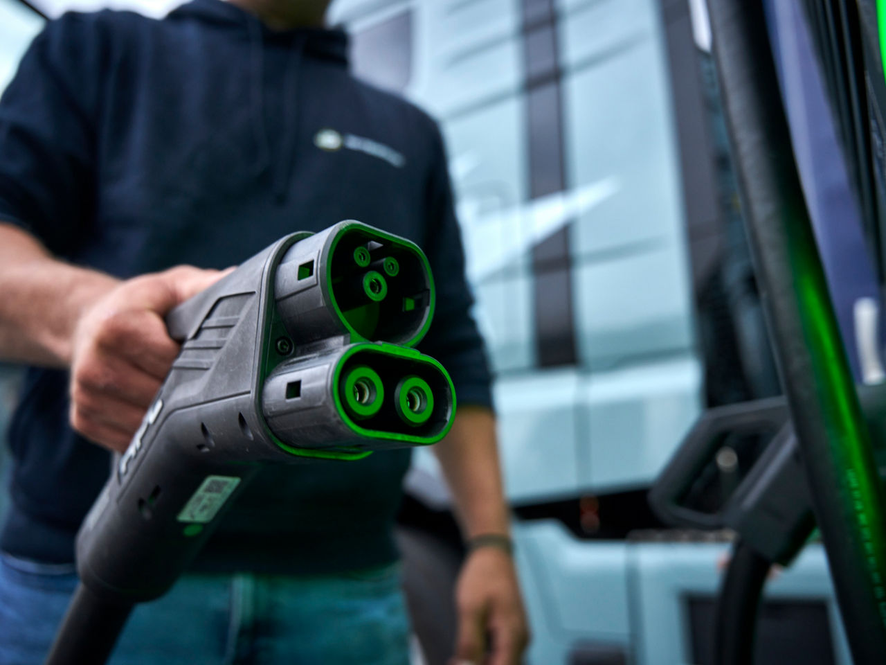 Ein Mann hält den Ladestecker, welcher zum Aufladen des eTrucks genutzt wird.