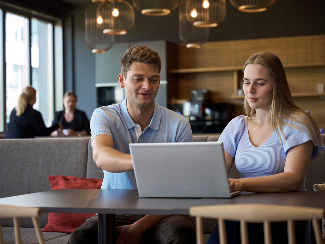 A young man and a young woman are sitting in front of a laptop while he is pointing at the screen