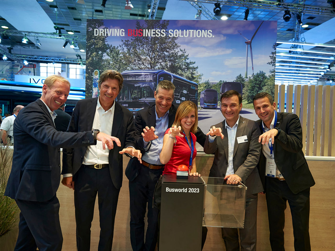 The satisfied MAN team in front of a large red buzzer at a booth