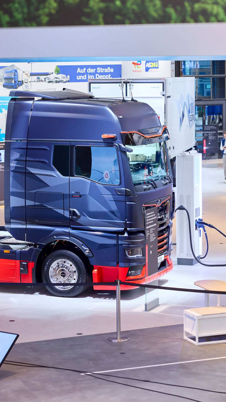 Ein MAN eTGX steht in einer Messehalle und hängt an einer Ladesäule