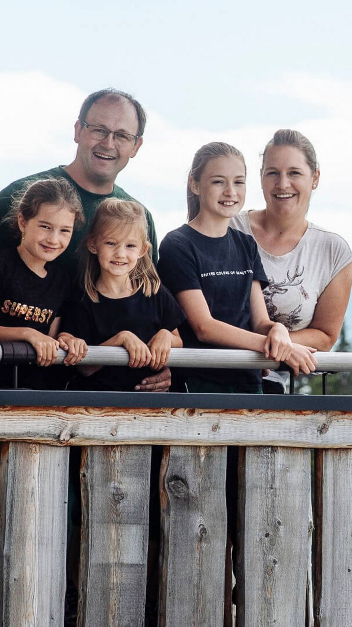 Familie steht auf dem Balkon ihrer Alm, hinter ihr die Berge