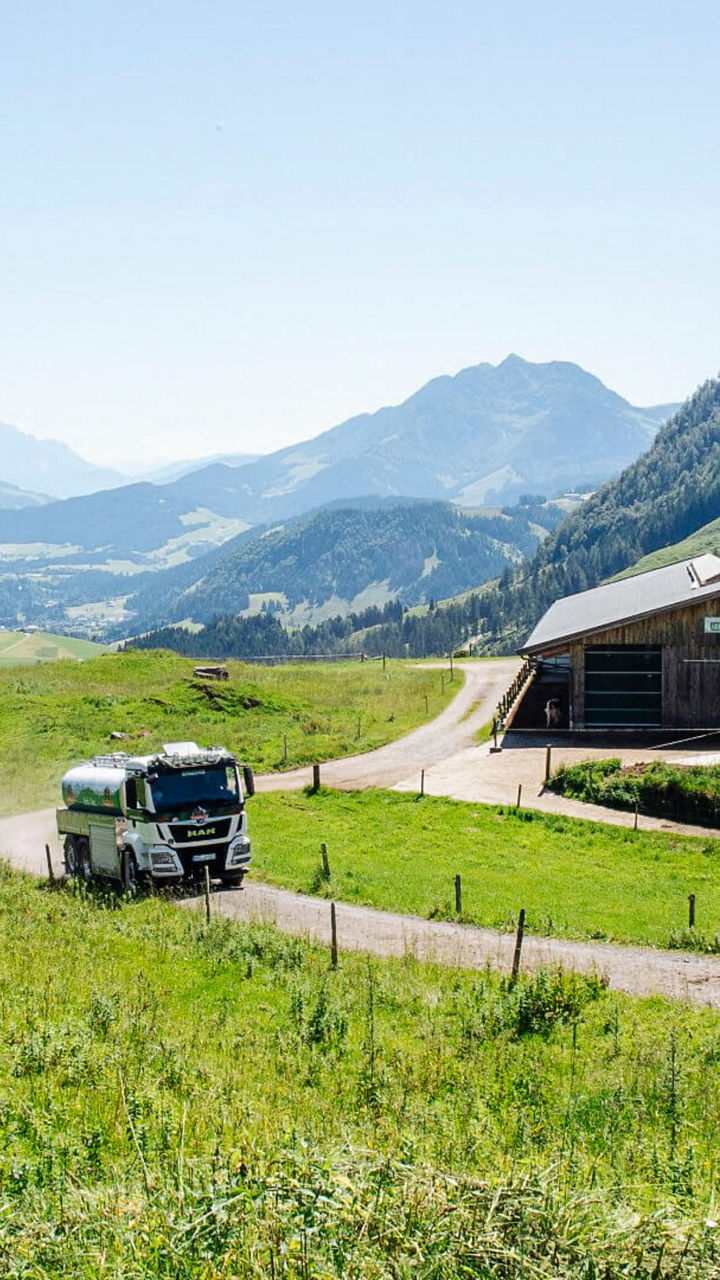 Blick über die Alm: Truck fährt an einer Almhütte vorbei