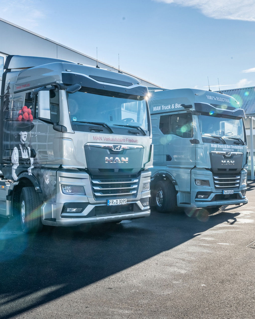 MAN TGX mit besonderen Airbrush und ein MAN eTGX nebeneinander vor dem MAN Servicebetieb.
