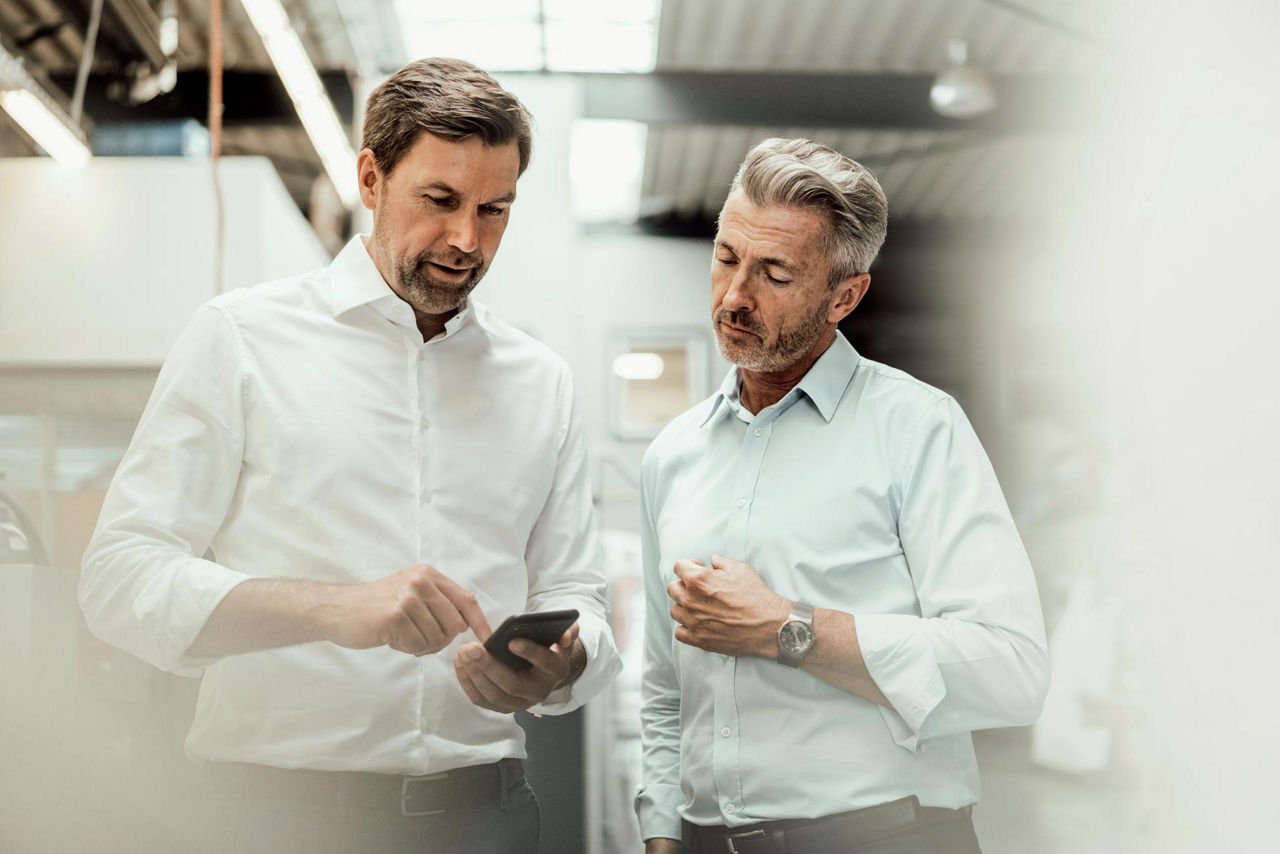Zwei Männer betrachten ein Smartphone in industrieller Umgebung