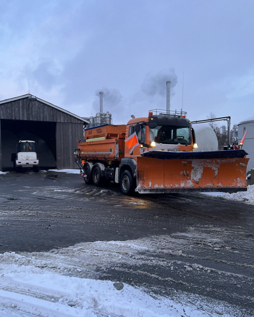 Ein oranger MAN Lkw im Winterdiensteinsatz mit montierten Schneeschiebeschild.