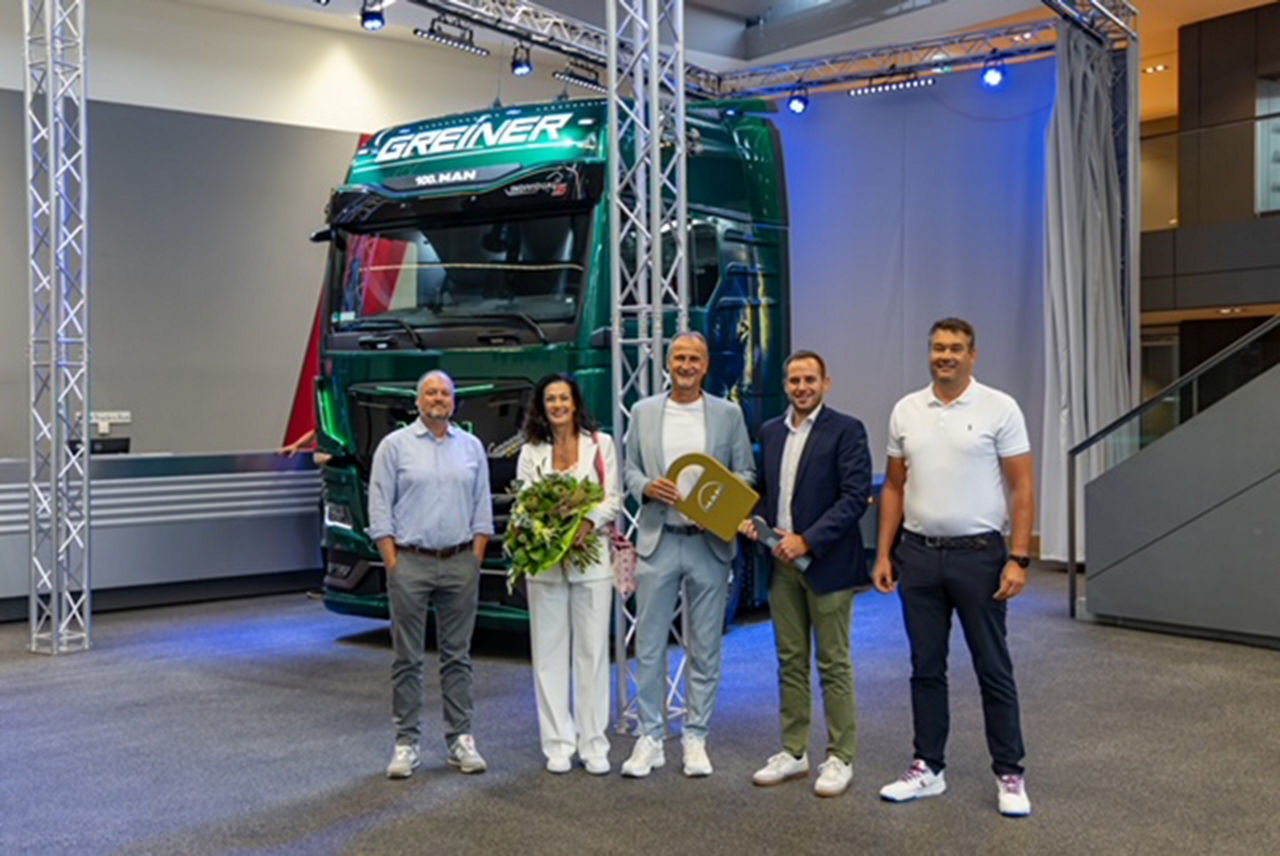 Übergabe des 100. MAN-Lkw an die Firma Erwin Greiner Kraftwagenspedition e.K. im MAN Truck Forum. Mehrere Personen stehen für das Übergabefoto vor dem Lkw.