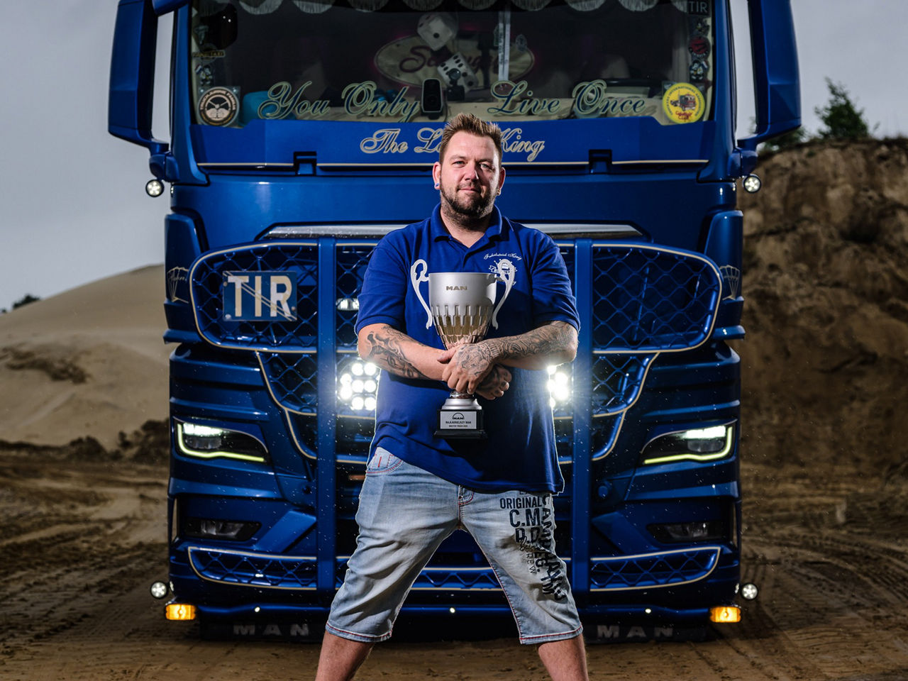 René Hintze steht vor seinem Lkw mit einem Pokal. Er gewinnt mit seinem blauen individuell gestalteten MAN TGX 18.510 den Titel „Schönster MAN 2025“ auf der Master Truck Show in Opole.