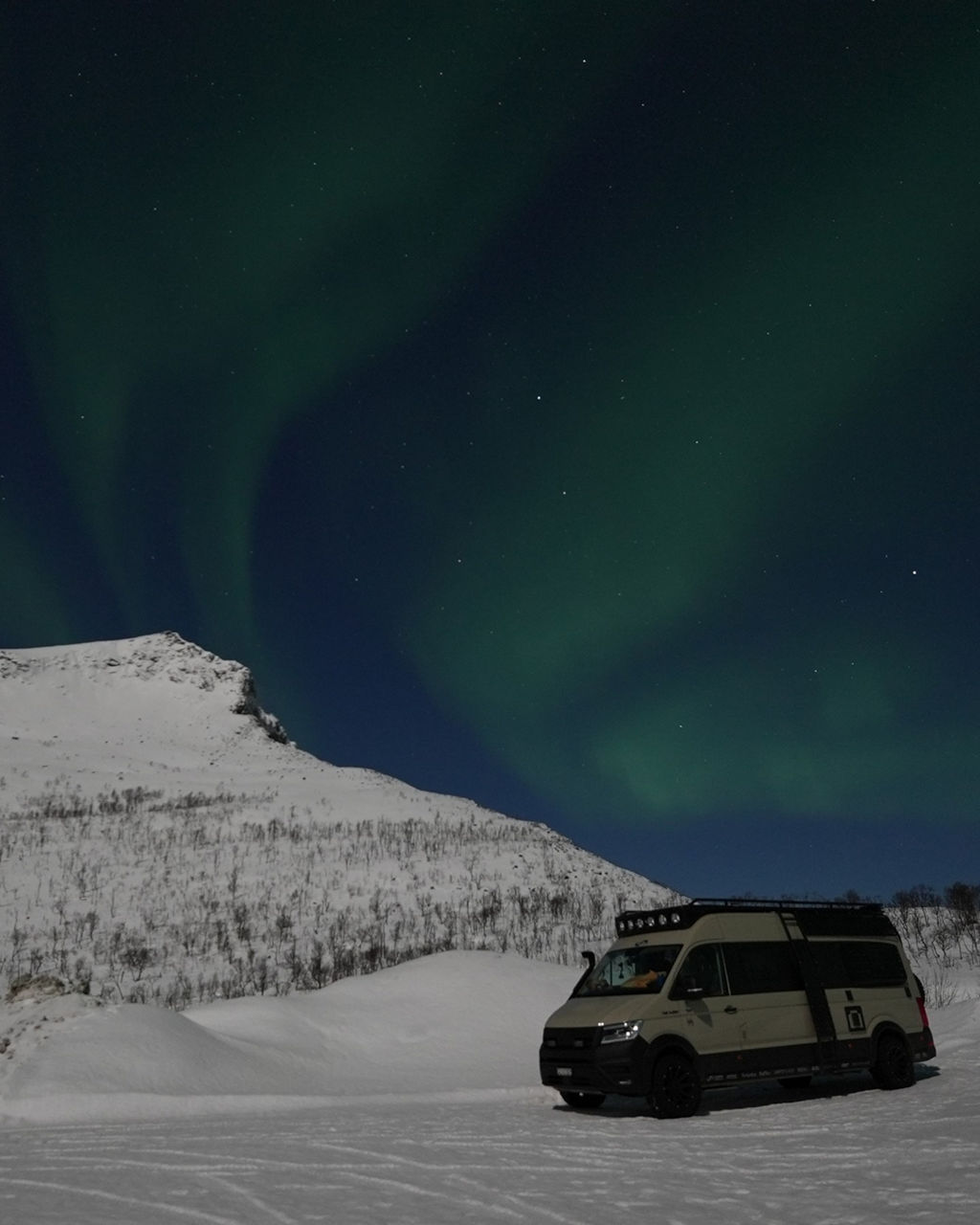 Kai Borstendorfer ist mit seinem MAN TGE im Norden von Europa unterwegs. Im Hintergrund sieht schneebedecke Berge und viele Polarlichter.