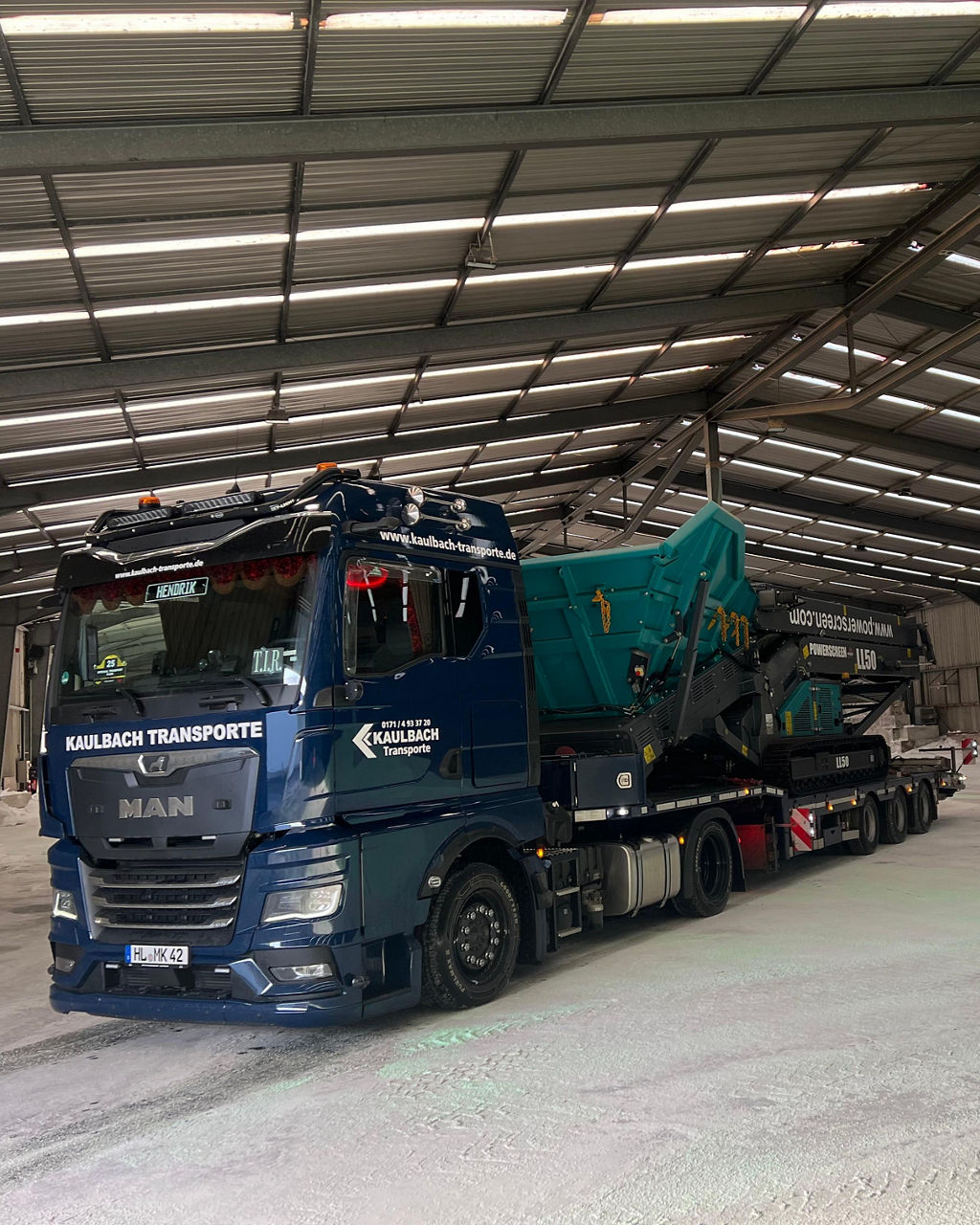 Der blaue MAN TGX von Michael Kaulbach transportiert eine große Maschine in eine Halle.