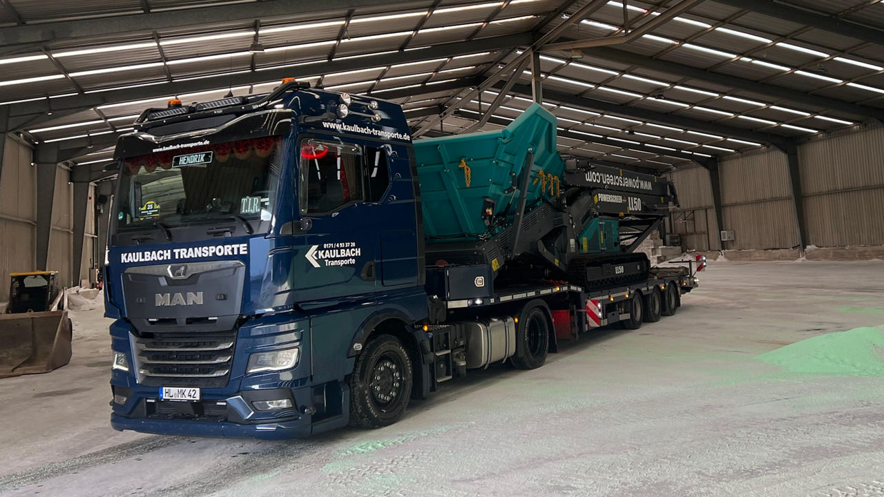 Der blaue MAN TGX von Michael Kaulbach transportiert eine große Maschine in eine Halle.