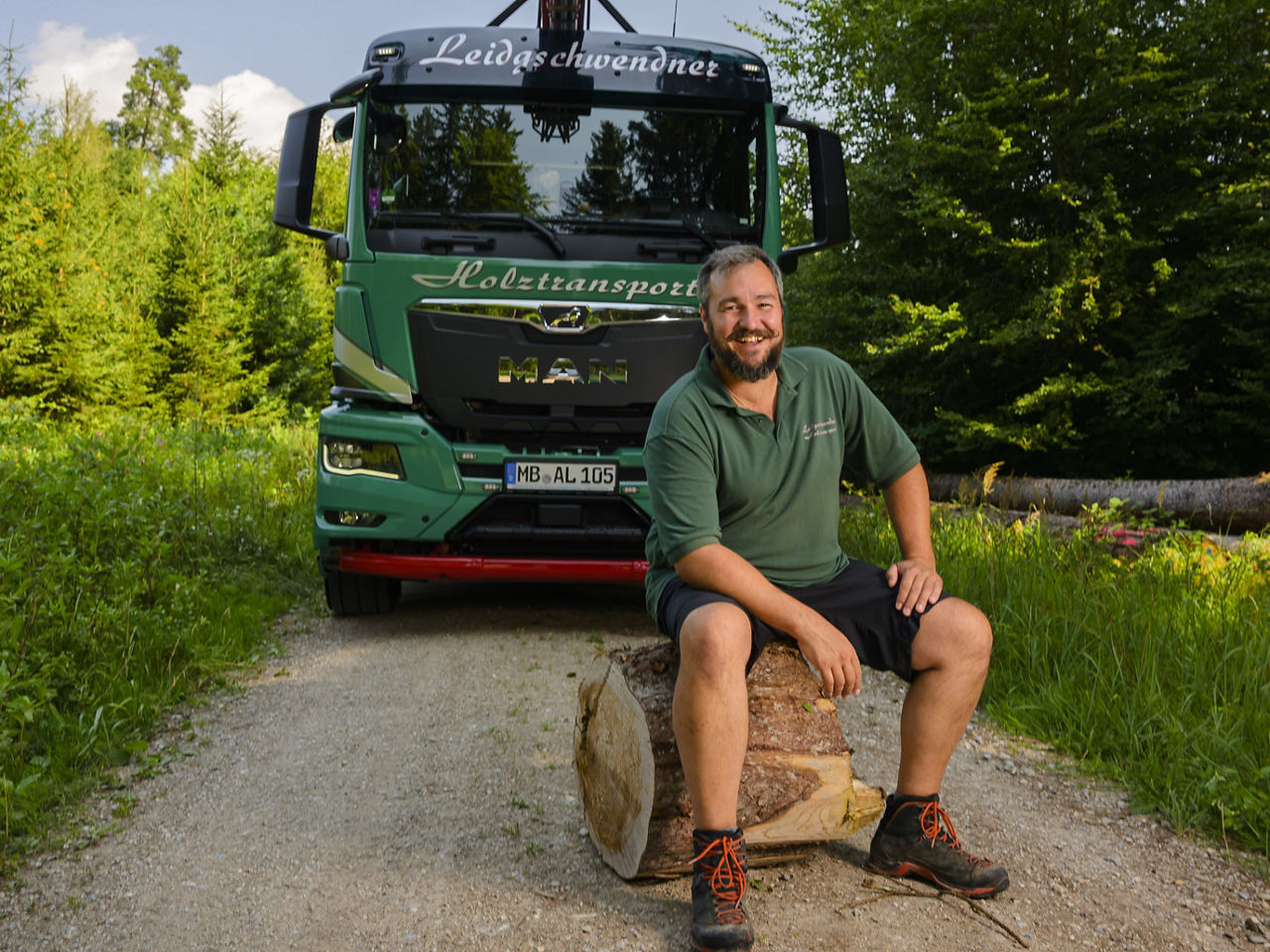 Andreas Leidgschwendner sitzt vor seinem MAN Holzzug, der voll beladen ist.
