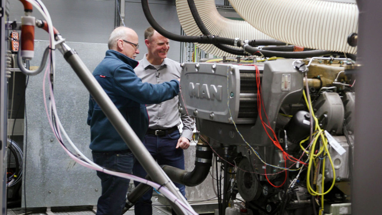 Two men are standing next to machine and are talking to each other.