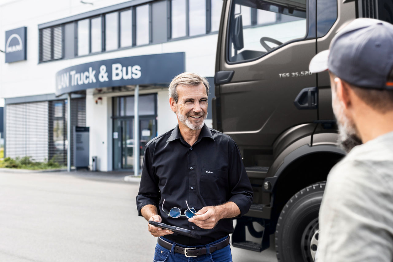 Zwei Männer stehen neben einem Lkw und unterhalten sich, wobei einer von ihnen ein Tablet in der Hand hält.