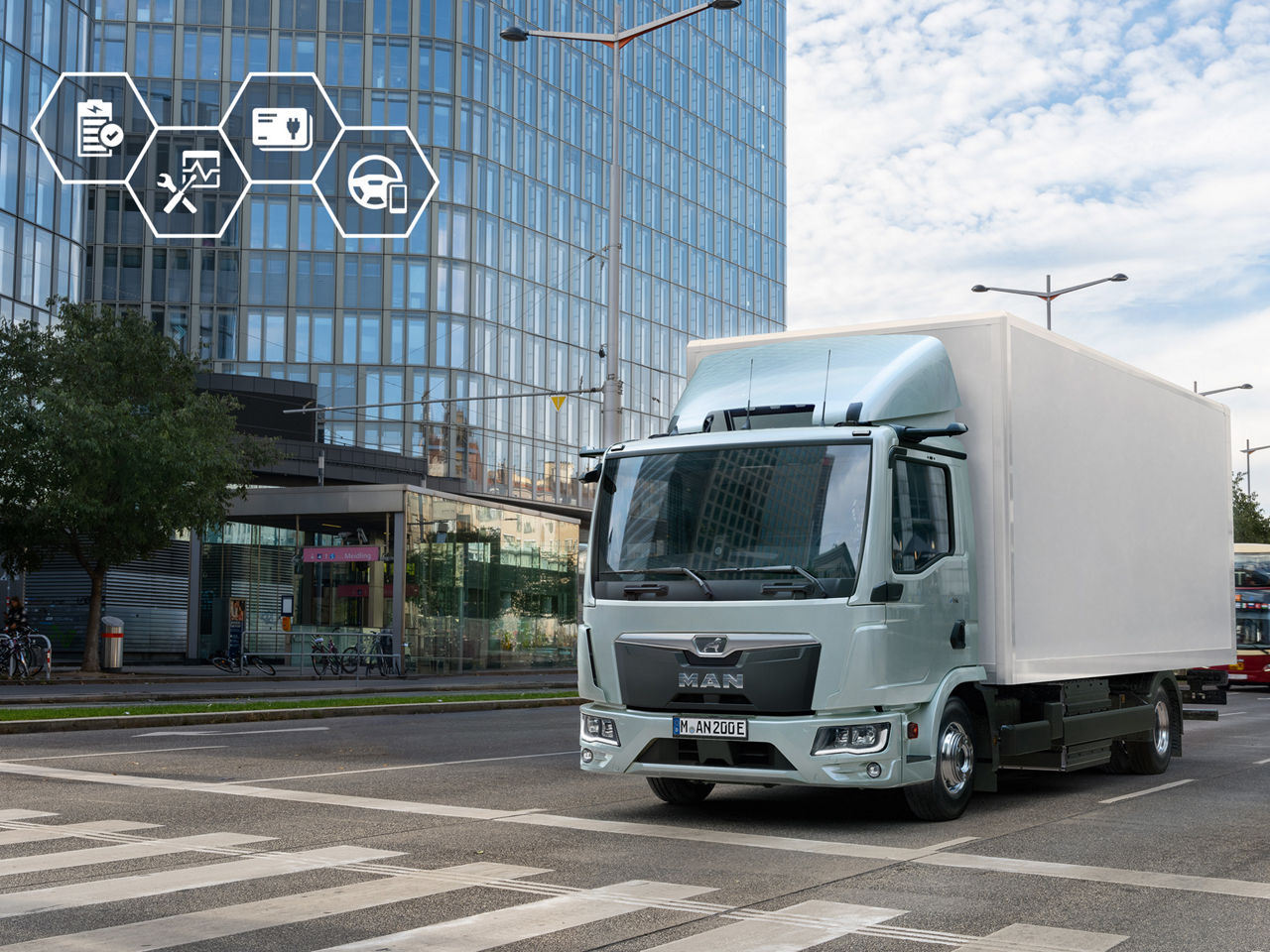 Elektrische MAN eTGL koelvrachtwagen rijdt door een stedelijke straat voor een modern kantoorgebouw.