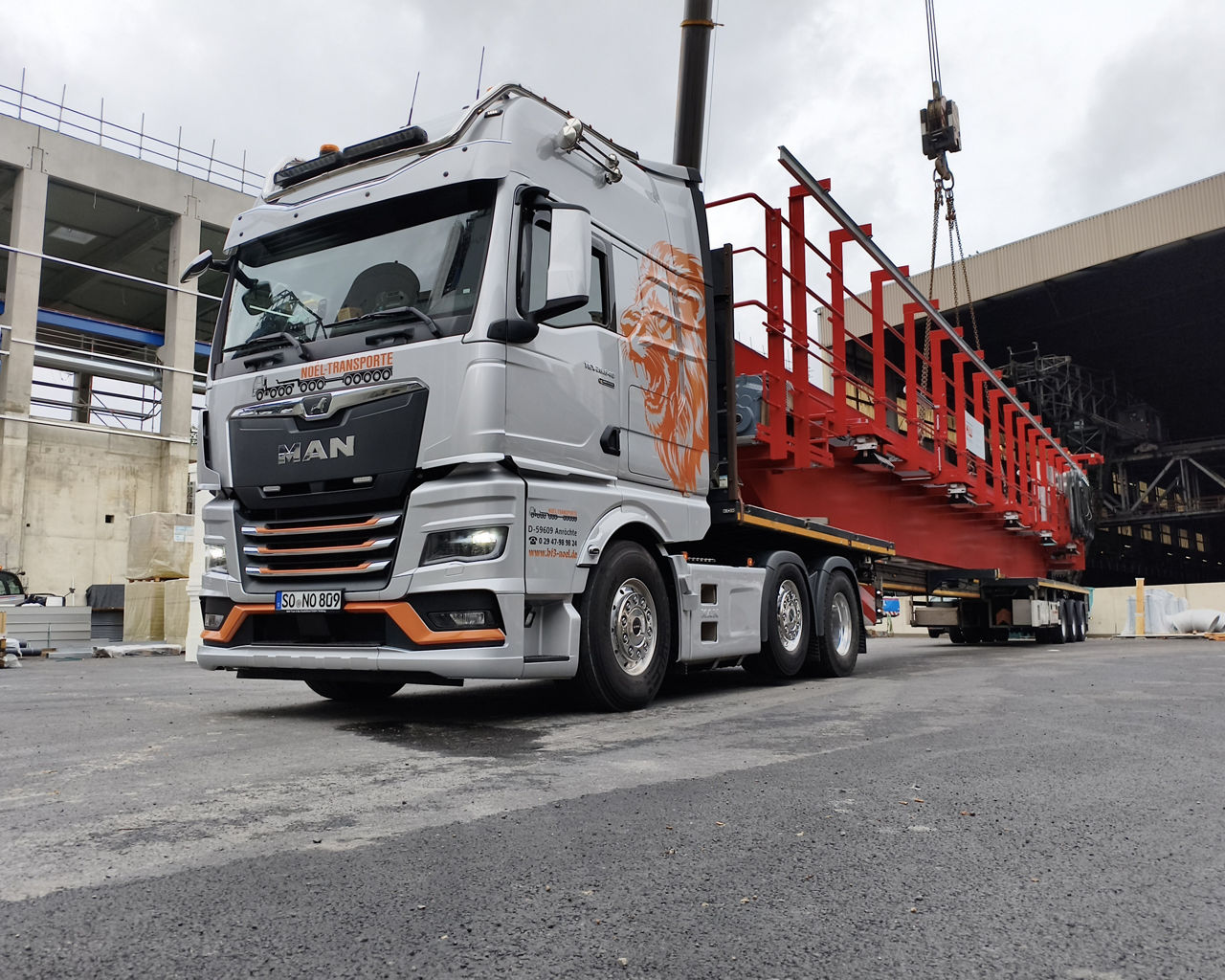 Der silberne MAN TGX transportiert einen Kran. 
