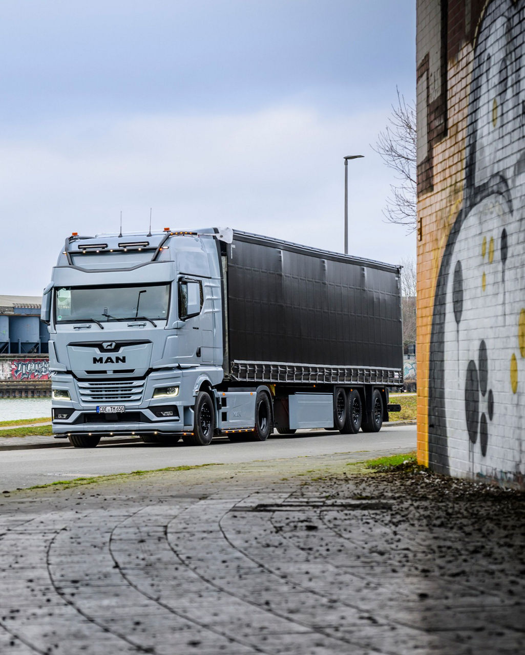 Ein grauer MAN TGX 18.560 mit D30-Motor fährt unter eine Unterführung mit Airbrush an den Wänden