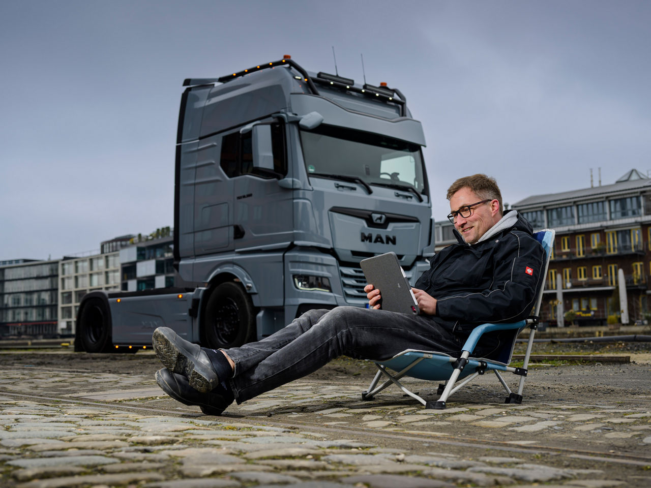 Ein grauer MAN TGX 18.560 mit D30-Motor steht vor Backsteingebäuden und sein Besitzer Tino Rateike sitzt vor dem Lkw.