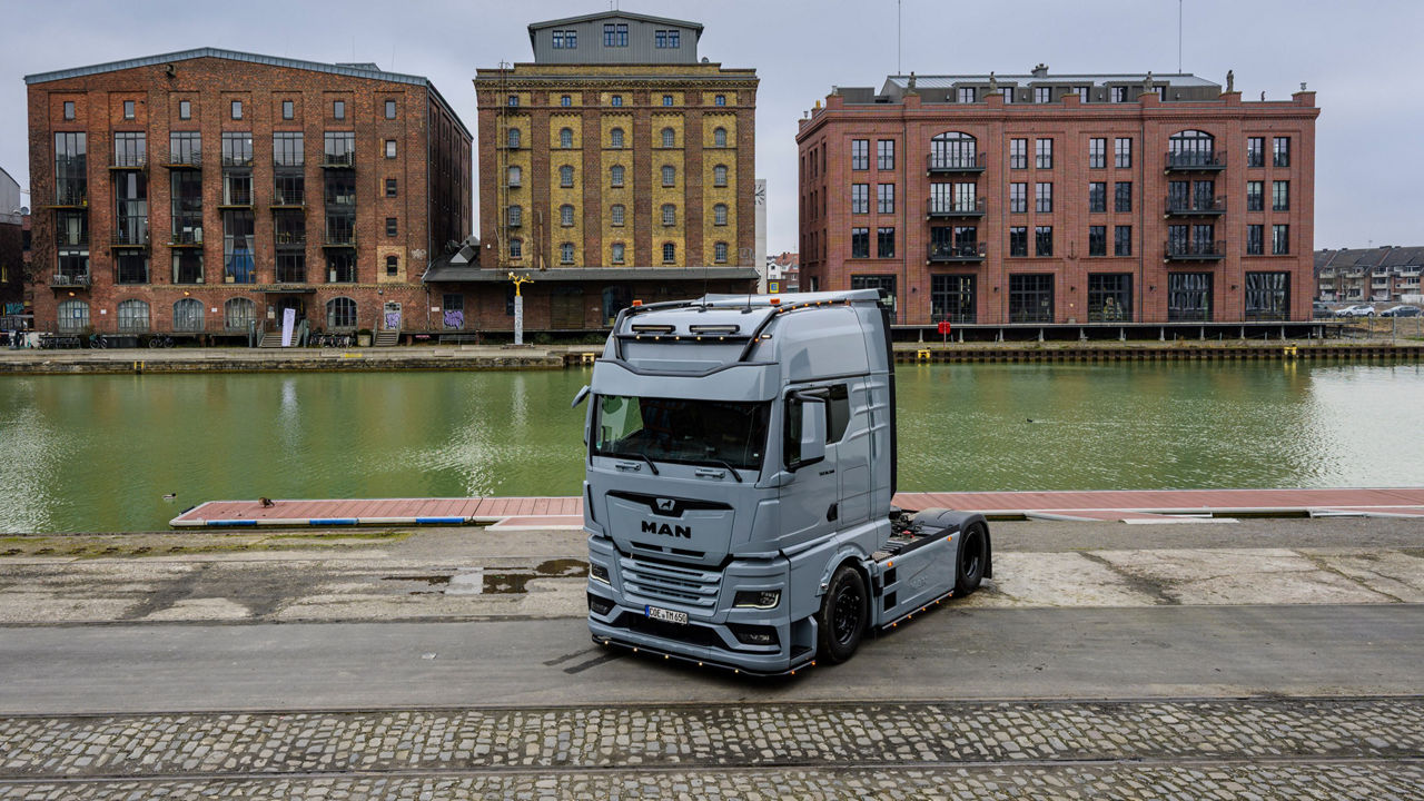 Ein grauer MAN TGX 18.560 mit D30-Motor steht vor Backsteingebäuden und sein Besitzer Tino Rateike lehnt am Lkw.