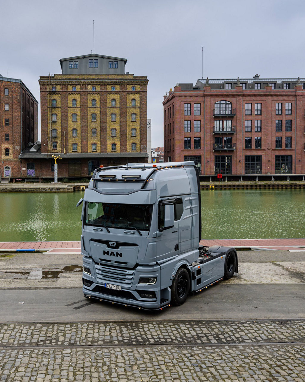 Ein grauer MAN TGX 18.560 mit D30-Motor steht vor Backsteingebäuden und sein Besitzer Tino Rateike lehnt am Lkw.