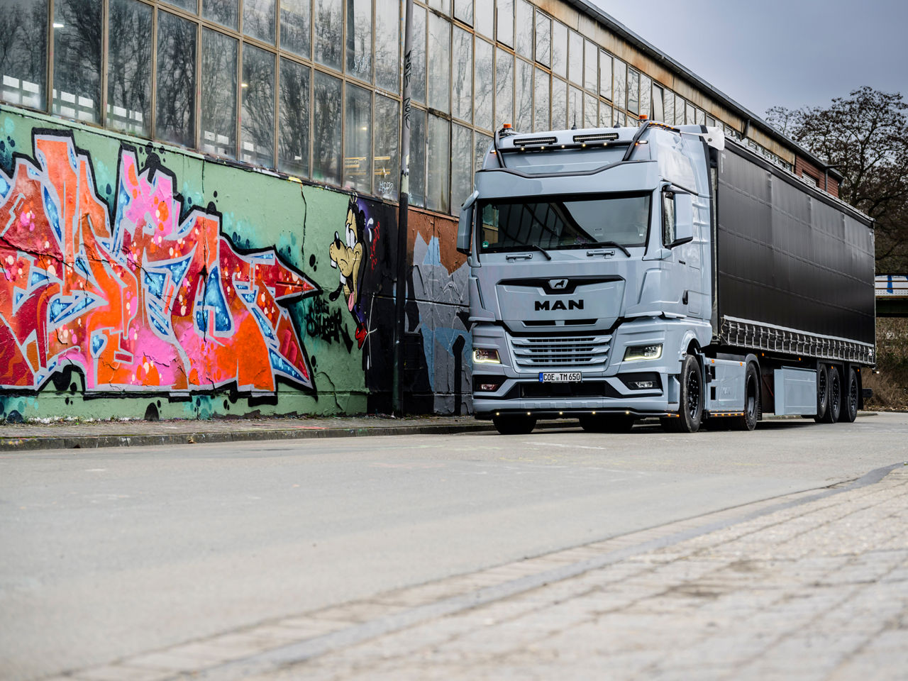 Ein grauer MAN TGX 18.560 mit D30-Motor von Tino Rateike fährt in ein altes Industrieviertel.