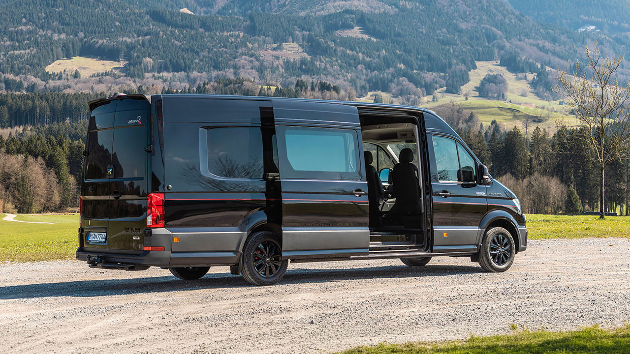 Schwarzes MAN TGE Reisemobil mit geöffneten Türen vor einer Berglandschaft.