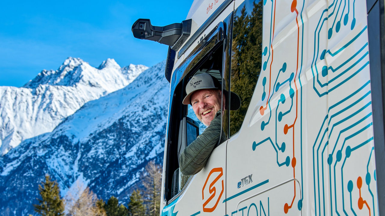 Christian Scheiber schaut aus dem MAN eTGX Fahrerfenster und hinter ihm erkennt man die Berge