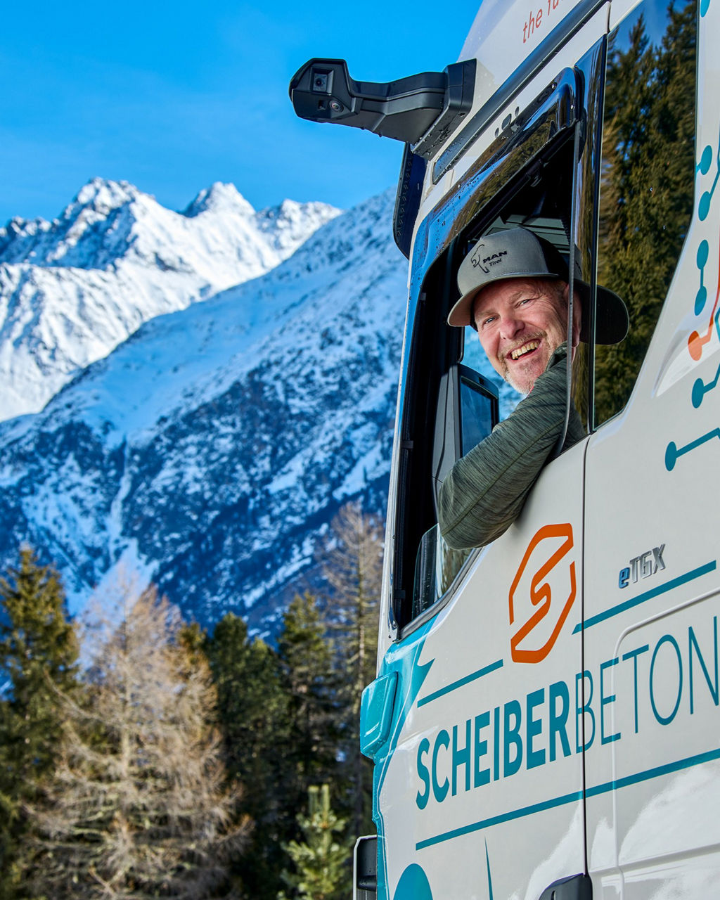Christian Scheiber schaut aus dem MAN eTGX Fahrerfenster und hinter ihm erkennt man die Berge
