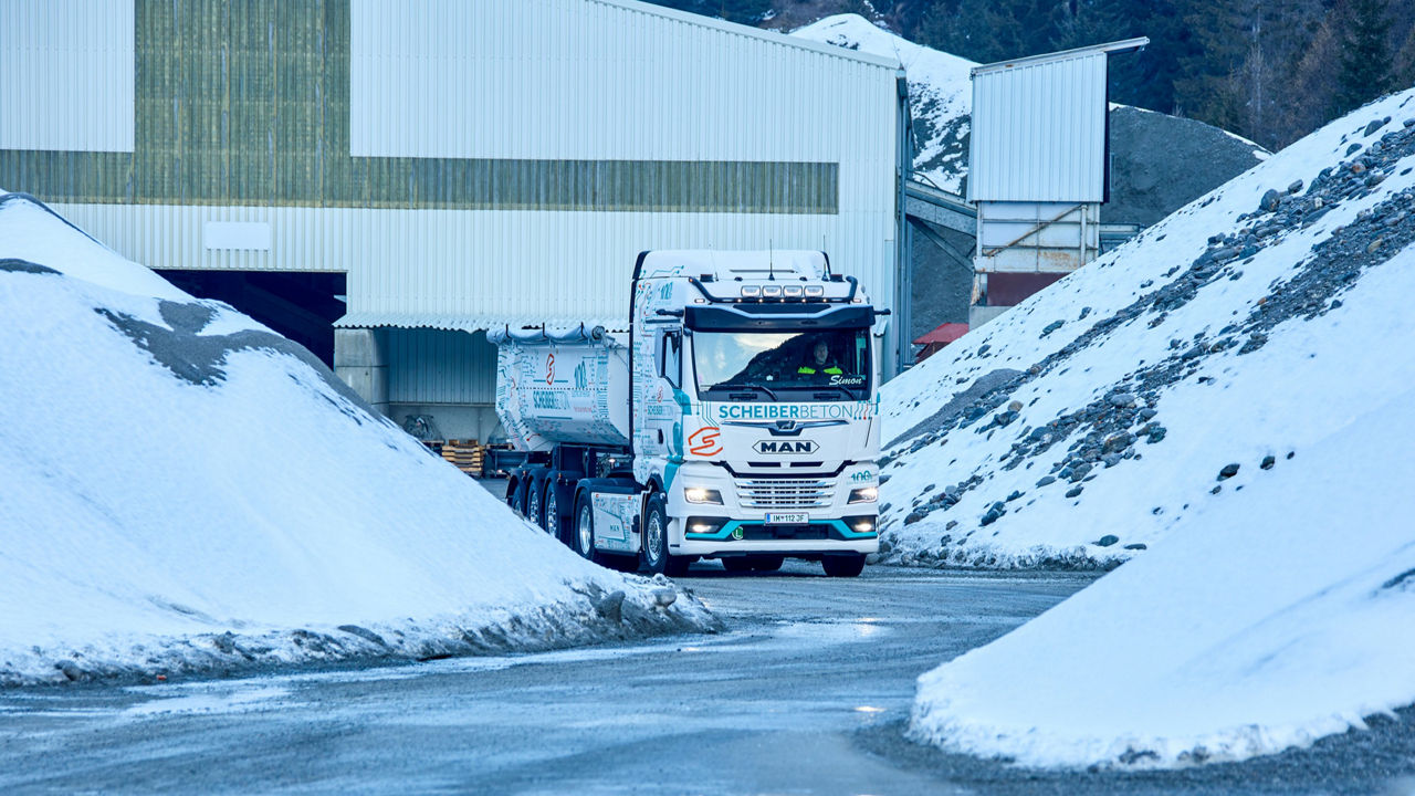 Der weiße MAN eTGX fährt an Schotterberge vorbei die noch mit Schnee bedeckt sind.