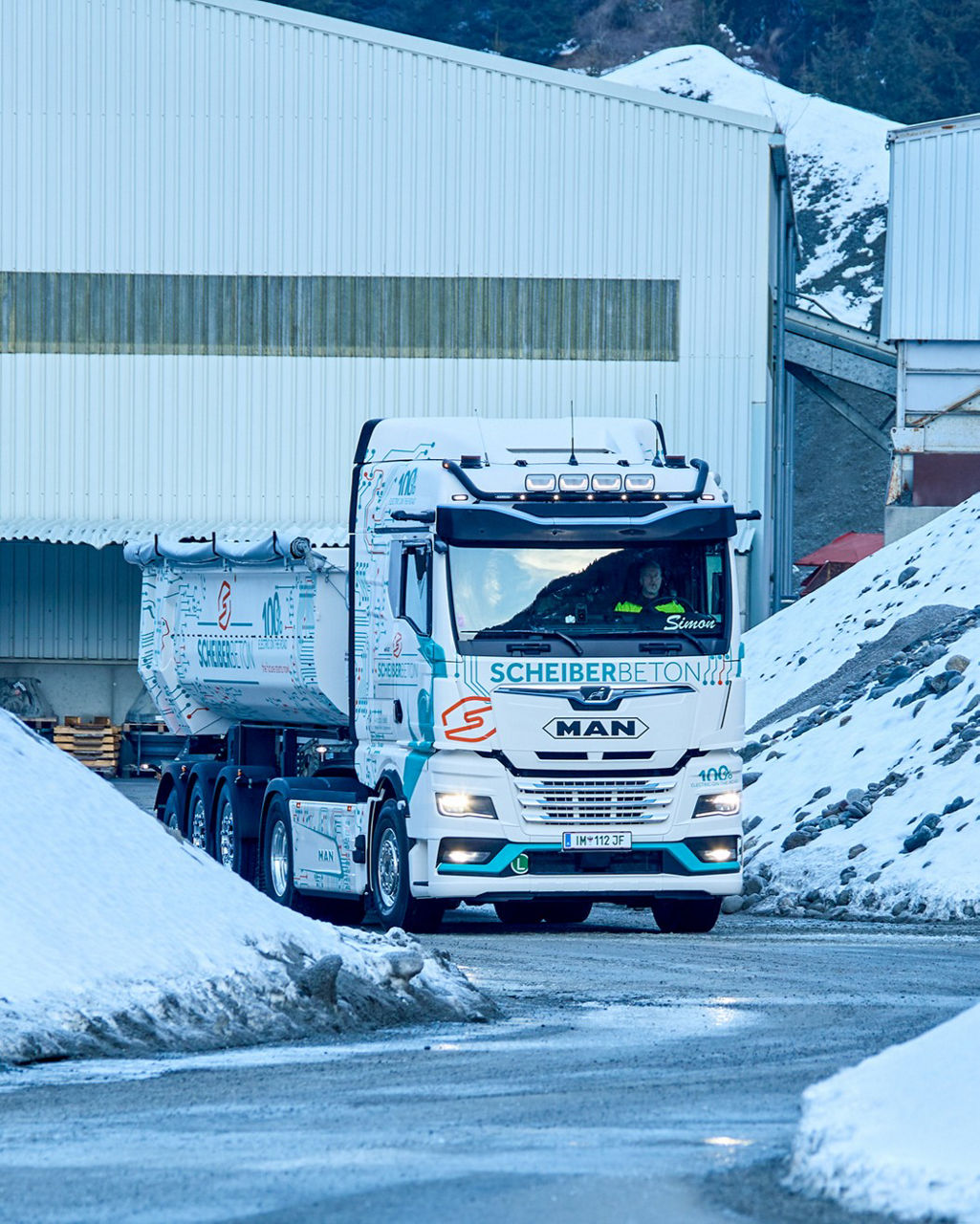 Der weiße MAN eTGX fährt an Schotterberge vorbei die noch mit Schnee bedeckt sind.