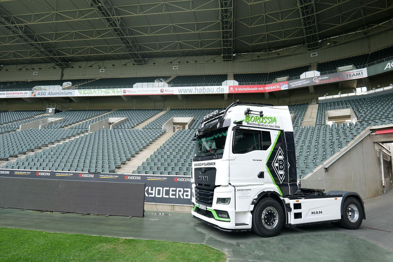 Ein weißer MAN TGX mit Borussia Mönchengladbach Beklebung und im Stadion von Borussia Mönchengladbach. Im Hintergrund sieht man die Ränge und Sitzplätze.