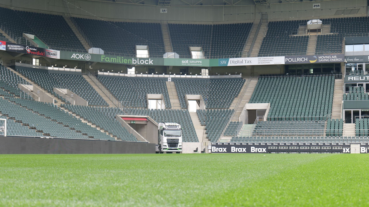 Ein weißer MAN TGX mit Borussia Mönchengladbach Beklebung und im Stadion von Borussia Mönchengladbach. Im Hintergrund sieht man die Ränge und Sitzplätze.