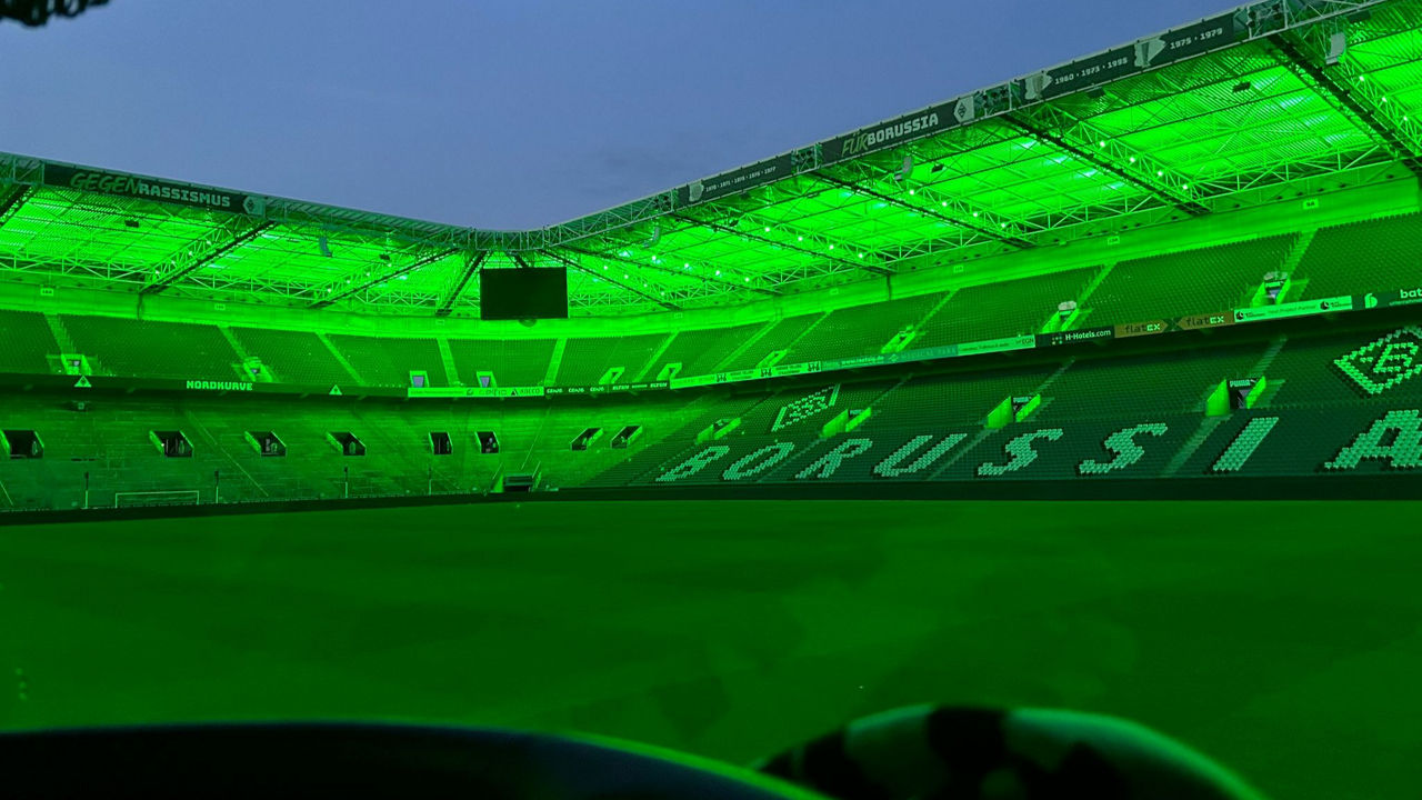Blick aus dem weißen MAN TGX in das grün beleuchtete Stadion und auf die Ränge.