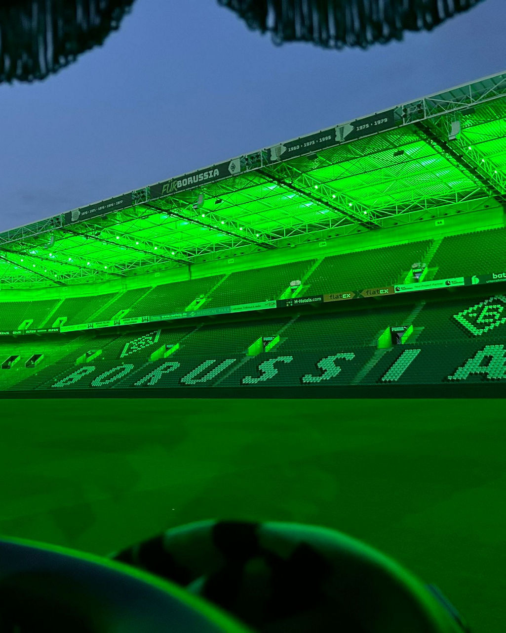 Blick aus dem weißen MAN TGX in das grün beleuchtete Stadion und auf die Ränge.