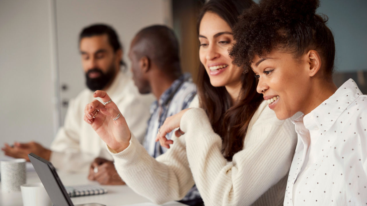 Several young professionals smiling and working together on a laptop