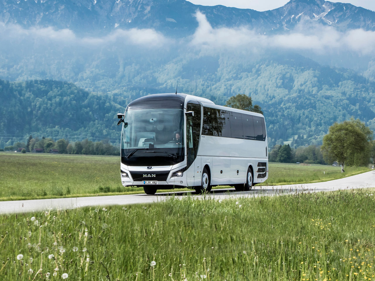 MAN Lion’s Coach driving down a road in front of a mountain panorama