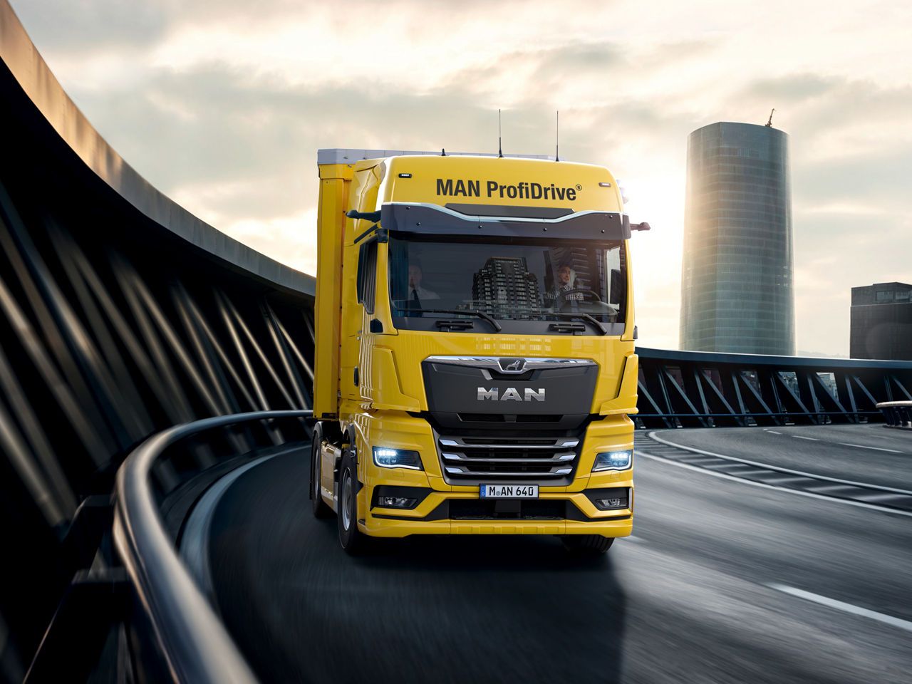 Ein gelber MAN TGX fährt auf einer Autobahn vor städtischer Kulisse